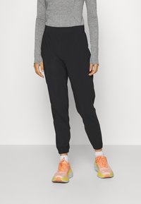 Pantaloni de sport negri cu manșete elastice, asortați cu un top lung cu mâneci gri deschis și adidași de alergare multiculoare. Țesătură netedă și ușoară.