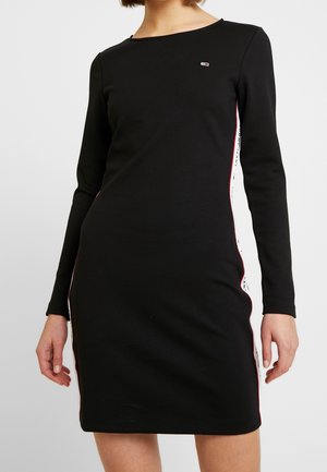 Robe noire ajustée à manches longues avec des rayures latérales blanches et rouges et un petit logo rectangulaire sur le haut de la poitrine.
