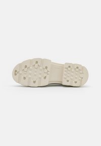 Shoe sole in off-white rubber with a textured design. Features multi-directional lugs and rounded edges for traction.