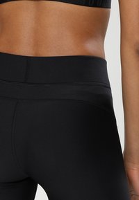 Černé vysoké legíny s hladkým povrchem, vybavené plochými švy a širokým pasem pro pohodlí a oporu.