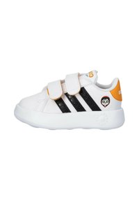Sneaker bianco con strisce nere, strap in velcro e dettagli arancioni. Presenta un tessuto strutturato e un motivo circolare sul tallone.