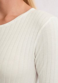 Haut à manches longues beige clair en tissu côtelé. Il présente un col rond et une texture subtile avec des lignes verticales.