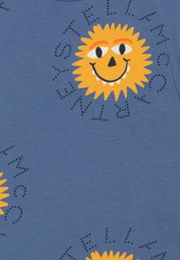 Tela de algodón azul con un gráfico de un sol sonriente amarillo con acentos naranjas, rodeado de letras punteadas que dicen "ESTELAR".