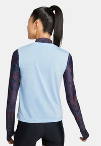 Top atlético sin mangas de color azul claro con un escote redondo, que presenta largas mangas con un patrón en azul oscuro y burdeos. Logo de Nike en el dobladillo.