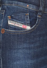Tmavě modré džíny z denimu s malou přední kapsou, šitím a viditelnou etiketou označenou "Diesel Industry Denim Division."