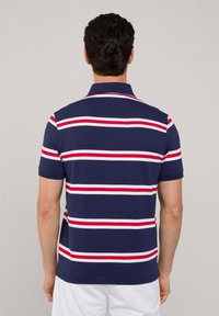 Polo de color azul marino con franjas horizontales rojas y blancas, mangas cortas y un cuello clásico. Material de algodón suave.