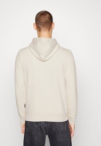 Felpa beige con una texture morbida, cappuccio regolabile e polsini a costine. Abbinata a jeans scuri in denim con tasche posteriori.
