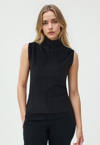 Zwarte mouwloze top met een opstaande kraag, voorzien van verticale ribbeltextuur en een strakke pasvorm, gecombineerd met zwarte broek.