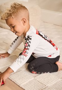 Pikad varrukad valge särk võidusõiduautode graafikaga ja ruuduline muster varrukatel, mustade retuusidega, millel on ruudulised aktsendid.