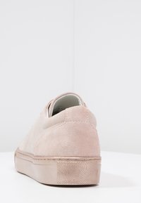 Basket en daim rose clair vue de l'arrière, avec des détails de couture et une semelle en caoutchouc texturée avec un léger talon surélevé.