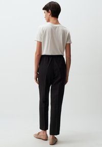 Zwarte elastische broek met een taps toelopende pijp. Gecombineerd met een lichtgekleurde t-shirt met korte mouwen. Glad materiaal, eenvoudig ontwerp.