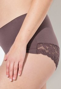 Mutandine a vita alta in un tessuto marrone tenue con pizzo floreale ai bordi delle gambe, caratterizzate da una texture liscia e un design aderente.