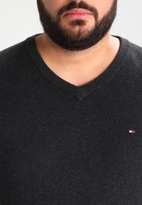 Svart v-ringad tröja i mjukt material. Har en liten röd, vit och blå logotyp på vänster bröst. Slät textur, lätt design.