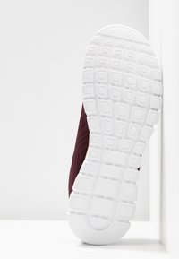 Baskets de sport bordeaux avec une tige en mesh texturé, semelle en caoutchouc blanc avec un motif en grille pour l'adhérence et un design à bout rond.