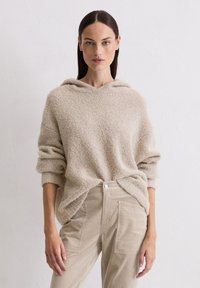 Felpa fuzzy beige con vestibilità ampia e coulisse, abbinata a pantaloni cargo beige chiaro con tasche laterali.