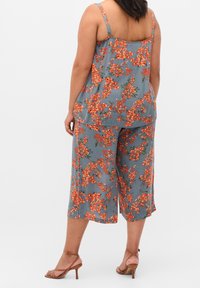 Blommig tvådelad outfit i grått tyg, med livfulla orange blommor. Ärmlös topp med breda cropped byxor, slät yta och spaghettiband.