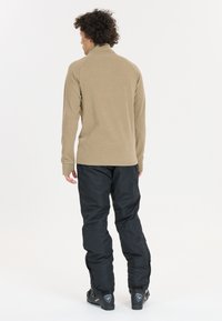 Tan langærmet top med høj hals, kombineret med sorte vandtætte bukser. Outfit'et har en afslappet pasform og slidstærkt stof.