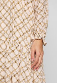 Light beige dress with a grid pattern in orange, blue, and white. Features gathered ruffle cuffs and pleats near the hem.