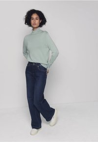 Světlé zelené rolákové tričko, tmavě modré džíny s širokými nohavicemi a bílé tenisky. Oblečení má volný střih a měkké textury.