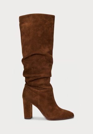 Stivale in suede marrone, alto fino al ginocchio, con un design svasato, punta affilata e tacco spesso. Dettaglio di cuciture sottili lungo le cuciture.