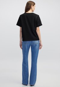 T-shirt nera a maniche corte, con dettagli borchiati sulle spalle. Abbinata a jeans in denim blu a gamba svasata. Tessuto morbido, vestibilità standard.
