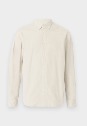 Srajca z dolgimi rokavi iz svetle bež tkanine, ki ima klasičen ovratnik in gumbasto zapiranje spredaj, s gladko teksturo.