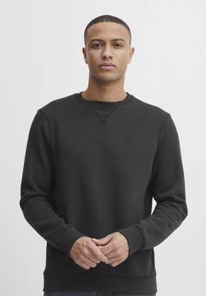 Zwarte ronde hals sweatshirt van zacht materiaal. Heeft een geribbelde textuur bij de halslijn en manchetten, met een klein logo op de borst.