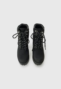 Bottines noires à lacets avec semelles épaisses et œillets en argent, montrées de haut sur un fond blanc.