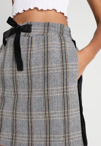 Jupe à motif pied-de-poule gris et noir avec un ruban noir à nouer à la taille, dotée de poches latérales et d'une coupe droite.