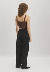 Brown ribbed crop top with wide straps paired with loose-fitting black cargo trousers featuring side pockets. Smooth texture with minimal detailing.
