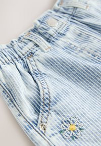 Shorts en denim bleu clair avec taille froncée, bouton en métal, poches avant et petit détail de fleur brodée blanche et jaune.