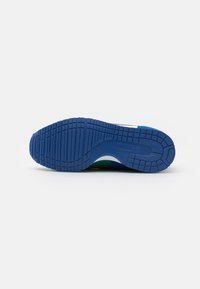 Semelle de sneaker en caoutchouc bleu avec un motif de traction texturé ; présente un bord blanc lisse et des accents verts près du talon.