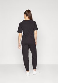 T-shirt de algodão preto com mangas curtas, combinado com calças de moletom pretas a condizer; apresenta um corte descontraído e detalhes mínimos. Ténis brancos visíveis.