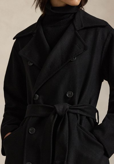 Černý dvouřadový kabát vyrobený z vlny, s velkými knoflíky, opaskem na úrovni pasu a širokým límcem. Hladká textura, dlouhé rukávy.
