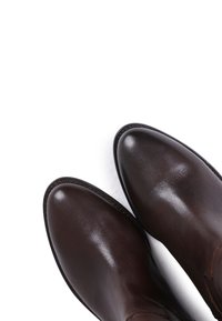 Chaussures en cuir marron avec un bout rond, texture lisse et détails de couture subtils le long du bord. La semelle semble robuste et légèrement brillante.
