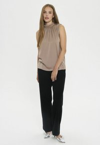 Top sin mangas color beige con escote plisado, combinado con pantalones negros y zapatos plateados de punta afilada. Tela suave con un ajuste cómodo.