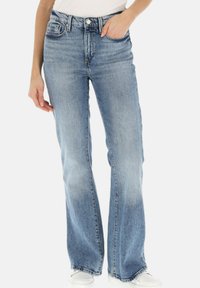 Jeans a zampa d'elefante blu chiaro in denim, con tasche anteriori, passanti per cintura e una finitura sbiadita. Indossati con sneakers bianche.