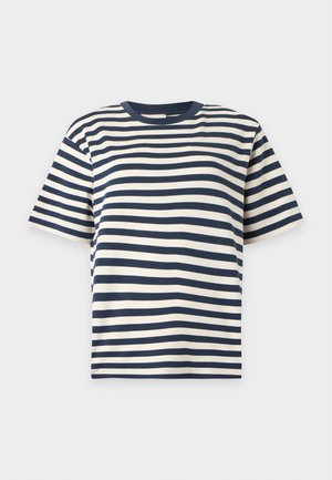 Kvinde stående iført en sort og hvid stribet T-shirt, et plisseret sennepsgul midilangt skørt og beige flade sko mod en ensfarvet baggrund.