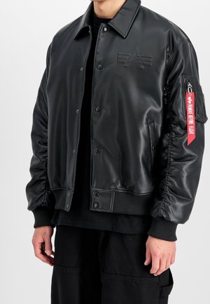 Czarna kurtka bomber z syntetycznej skóry z zatrzaskami, ściągaczami na mankietach, kieszenią na ramieniu z czerwoną zawieszką „Remove Before Flight” oraz tłoczonym logo na piersi.