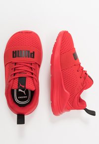 Chaussures de sport rouges avec une tige en maille respirante, cheville rembourrée et sangle réglable. Comprend un marquage noir et une semelle en caoutchouc texturé.