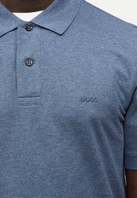 Μπλε υφασμάτινο πόλο με κοντά μανίκια, δύο σκούρα κουμπιά και κέντημα “BOSS” στο αριστερό στήθος.