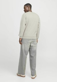 Lichtgrijze sweatshirt met ronde hals en geribde manchetten, gecombineerd met losse lichtblauwe spijkerbroeken. Minimalistisch ontwerp, geen zichtbare patronen.