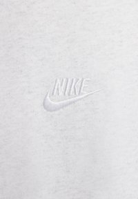 Witte stof met een zachte textuur; heeft een geborduurd wit Nike-logo in het midden, dat de merknaam en het swoosh-ontwerp toont.