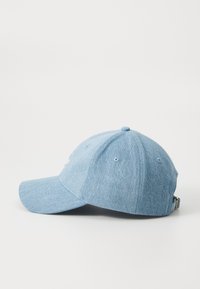 Cappellino da baseball in denim blu con visiera curva, sei fori di ventilazione e una fascia regolabile. Presenta una cucitura sottile sul davanti.
