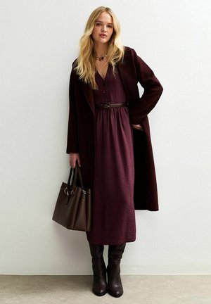 Robe longue bordeaux avec une ceinture, accompagnée d'un manteau assorti. Sac à main marron et bottes hautes viennent compléter le look. Texture lisse et design élégant.