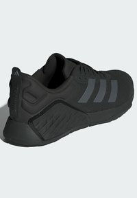 Chaussure de sport noire avec une tige texturée, un talon renforcé, trois bandes grises et une semelle en caoutchouc à motifs, conçue pour la stabilité pendant l'entraînement.