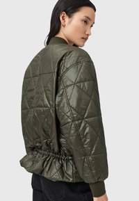 Quilted olivenfarvet bomberjakke med en glat finish, samlet kant og ribbede cuffs. Har diamantmønstre på stoffet.