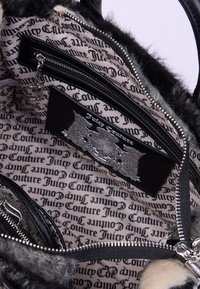 Interno della borsa nera con accessori in argento, caratterizzato da un bordo in pelliccia sintetica. Foderato con tessuto a fantasia di Juicy Couture e scomparti con zip.