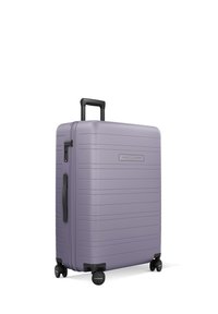 Valise rigide de couleur violet clair avec des rainures horizontales, poignée intégrée, accents noirs et quatre roues pour la mobilité.