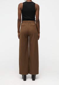 Pantalons larges marron à taille haute, avec une taille élastique et deux poches arrière, associés à un haut noir sans manches.
